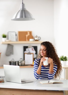 kahve fincanı ve dizüstü evde mutfakta gülümseyen genç kadın
