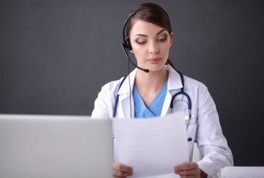 Kulaklık takan doktor dizüstü bilgisayarlı bir masanın arkasında oturuyor.