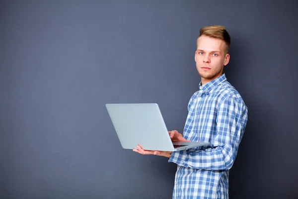 Giovane uomo in piedi e utilizzando computer portatile isolato su uno sfondo grigio — Foto Stock