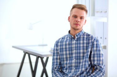 Genç işadamı ofiste çalışıyor, masada oturuyor.