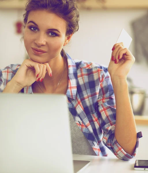 Mujer sonriente compras en línea utilizando la computadora y la tarjeta de crédito en la cocina —  Fotos de Stock