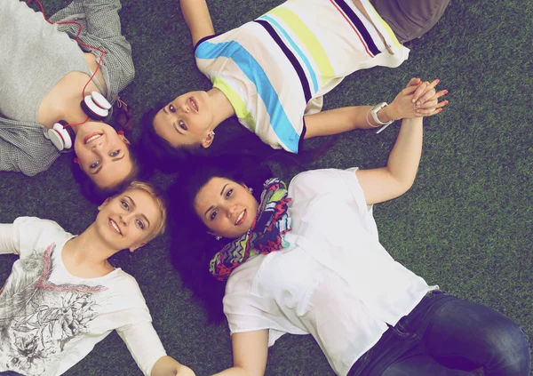 Quatro mulheres jovens deitadas na grama verde — Fotografia de Stock