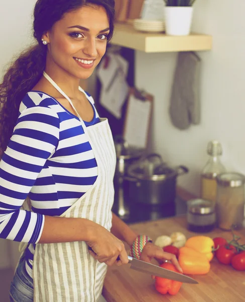 Jovem mulher cortando legumes na cozinha, de pé perto da mesa — Fotografia de Stock