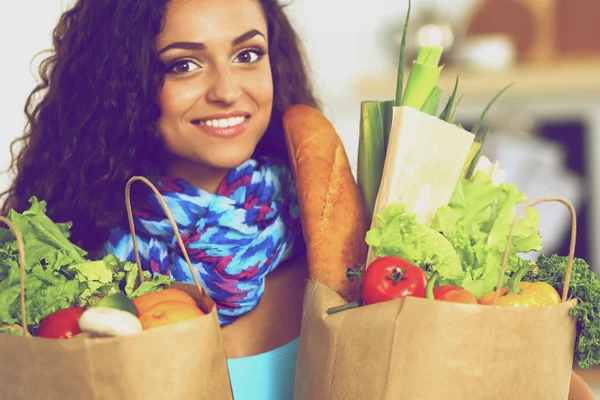 Mujer joven sosteniendo bolsa de la compra de comestibles con verduras de pie en la cocina — Foto de Stock