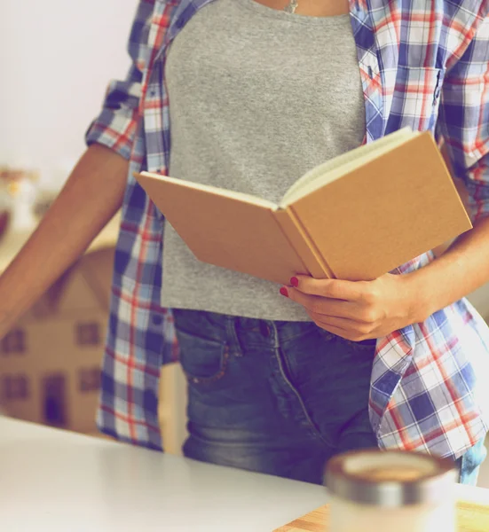 Mujer joven leyendo libro de cocina en la cocina, buscando receta — Foto de Stock