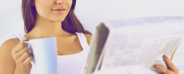 Una hermosa joven leyendo el periódico en la cama y disfrutando de una taza de té — Foto de Stock