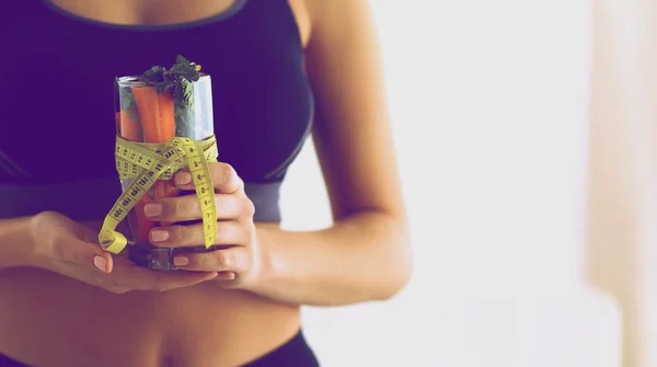 Mujer sosteniendo un vaso lleno de ensalada de frutas frescas con una cinta métrica alrededor del vaso — Foto de Stock