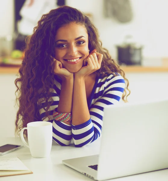 Giovane donna sorridente con tazza di caffè e laptop in cucina a casa — Foto Stock