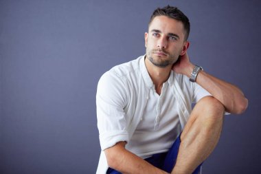 Gri arka planda yalnız oturan genç iş adamı.