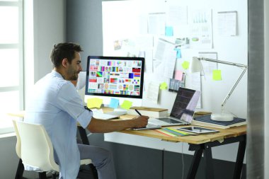 İnternette çalışırken bilgisayarın ve dizüstü bilgisayarın önünde grafik stüdyosunda oturan genç tasarımcının portresi.