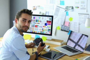 İnternette çalışırken bilgisayarın ve dizüstü bilgisayarın önünde grafik stüdyosunda oturan genç tasarımcının portresi.