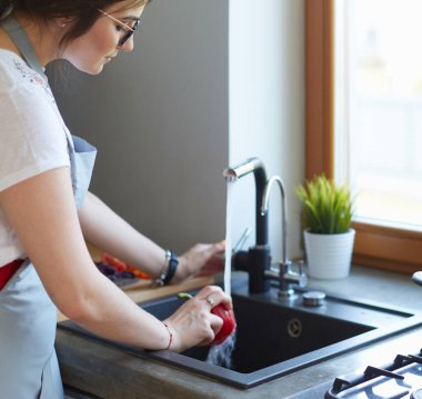 Sebze yıkayan kadın. Güzel genç bir kadın salata için sebze yıkıyor ve mutfakta dururken gülümsüyor.