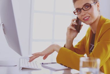 İş kadını ofiste bilgisayar ve cep telefonu kullanarak işine konsantre oluyor.