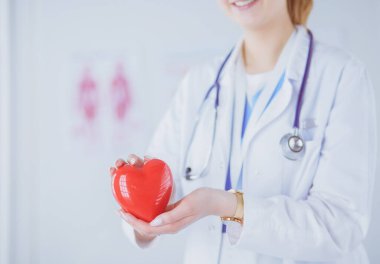 Steteskop tutan, kalbi hafif arka planda olan kadın bir doktor.