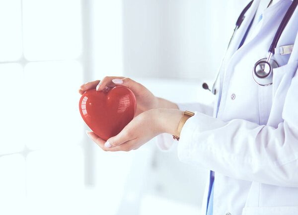 Женщина-врач со стетоскопом, держащая сердце на светлом фоне