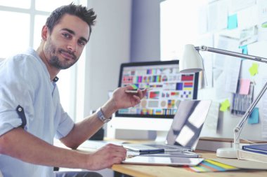 İnternette çalışırken bilgisayarın ve dizüstü bilgisayarın önünde grafik stüdyosunda oturan genç tasarımcının portresi.