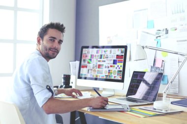 İnternette çalışırken bilgisayarın ve dizüstü bilgisayarın önünde grafik stüdyosunda oturan genç tasarımcının portresi.