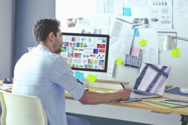 İnternette çalışırken bilgisayarın ve dizüstü bilgisayarın önünde grafik stüdyosunda oturan genç tasarımcının portresi.