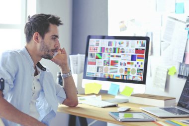 İnternette çalışırken bilgisayarın ve dizüstü bilgisayarın önünde grafik stüdyosunda oturan genç tasarımcının portresi.