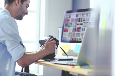 İnternette çalışırken bilgisayarın ve dizüstü bilgisayarın önünde grafik stüdyosunda oturan genç tasarımcının portresi.