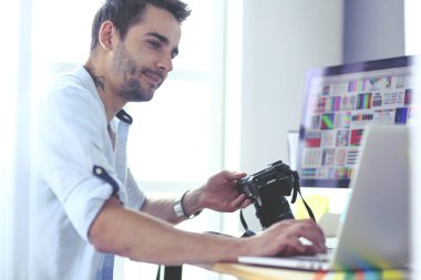 İnternette çalışırken bilgisayarın ve dizüstü bilgisayarın önünde grafik stüdyosunda oturan genç tasarımcının portresi.