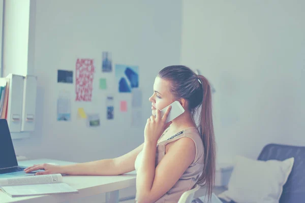 Młoda bizneswoman siedzi przy biurku i rozmawia przez telefon — Zdjęcie stockowe