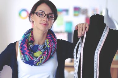 Gülümseyen moda tasarımcısı ofiste mankenin yanında duruyor.