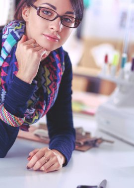 Güzel moda tasarımcısı stüdyoda masada oturuyor.