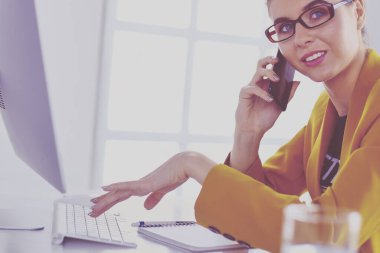 İş kadını ofiste bilgisayar ve cep telefonu kullanarak işine konsantre oluyor.