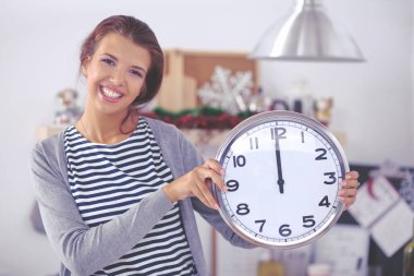 Mutlu genç kadın Noel süslemeli mutfakta saat gösteriyor.