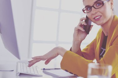 İş kadını ofiste bilgisayar ve cep telefonu kullanarak işine konsantre oluyor.