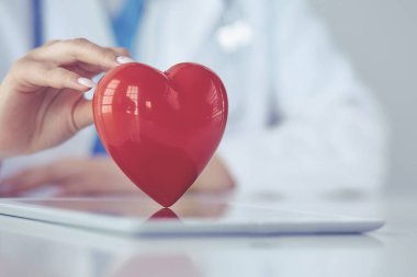 Steteskop tutan, kalbi hafif arka planda olan kadın bir doktor.