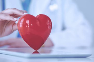 Steteskop tutan, kalbi hafif arka planda olan kadın bir doktor.