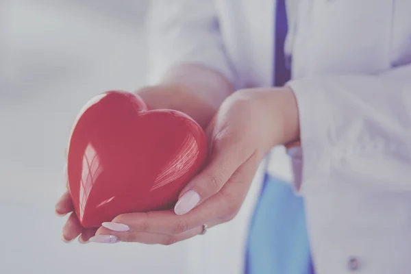 Medico femminile con stetoscopio che tiene il cuore, su sfondo chiaro — Foto Stock