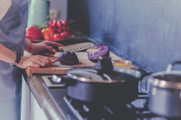 Junge Frau schneidet Gemüse in Küche neben Schreibtisch — Stockfoto