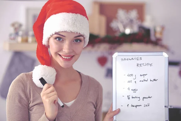 Glimlachende jonge vrouw in de keuken, geïsoleerd op kerst achtergrond — Stockfoto