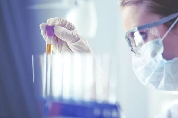 Een medisch of wetenschappelijk onderzoeker of arts die in een laboratorium naar een reageerbuis met vloeibare groene oplossing kijkt — Stockfoto