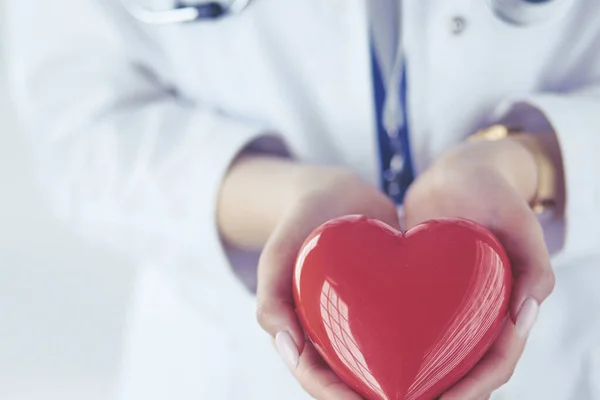 Medico femminile con stetoscopio che tiene il cuore, su sfondo chiaro — Foto Stock