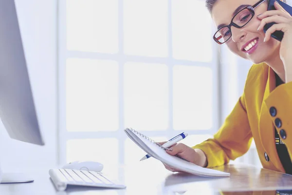 Portret van een mooie vrouw die belt terwijl ze op haar werkplek voor de laptop zit en aan een nieuw project werkt — Stockfoto