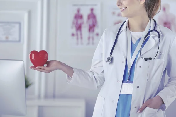 Medico femminile con stetoscopio che tiene il cuore, su sfondo chiaro — Foto Stock