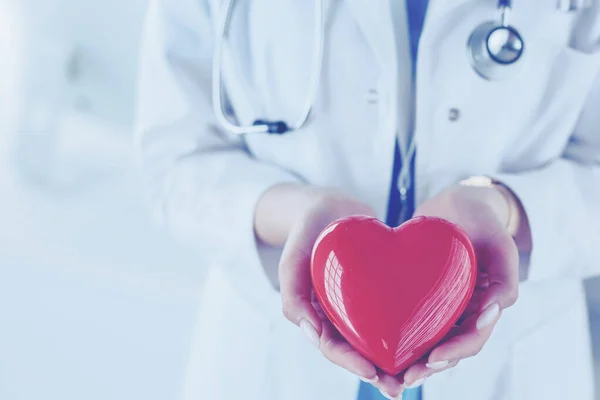 Female doctor with stethoscope holding heart, on light background — Stock Photo, Image