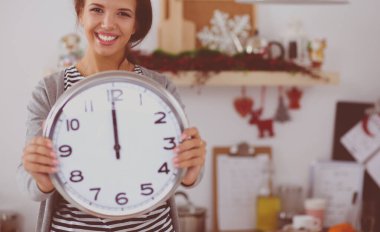 Mutlu genç kadın Noel süslemeli mutfakta saat gösteriyor.