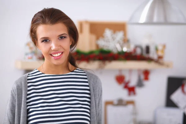 Glimlachende jonge vrouw in de keuken, geïsoleerd op kerst achtergrond — Stockfoto