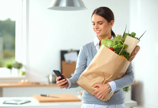 Mladá žena drží nákupní tašku se zeleninou. Stojí v kuchyni — Stock fotografie