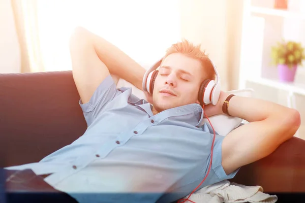 Een jonge knappe man op de bank luisterend naar muziek — Stockfoto