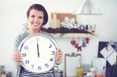 Mutlu genç kadın Noel süslemeli mutfakta saat gösteriyor.