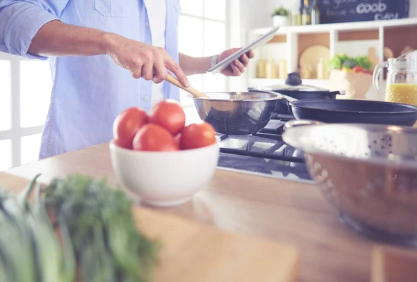 Man following recipe on digital tablet and cooking tasty and healthy food in kitchen at home — Stock Photo, Image