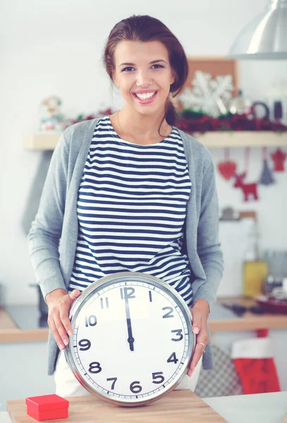Retrato de una joven sonriente sosteniendo el reloj en la cocina decorada con navidad —  Fotos de Stock