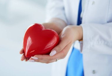 Steteskop tutan, kalbi hafif arka planda olan kadın bir doktor.