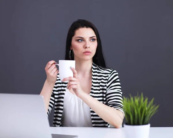 Jonge vrouw met een laptop zitten geïsoleerd op grijze achtergrond — Stockfoto